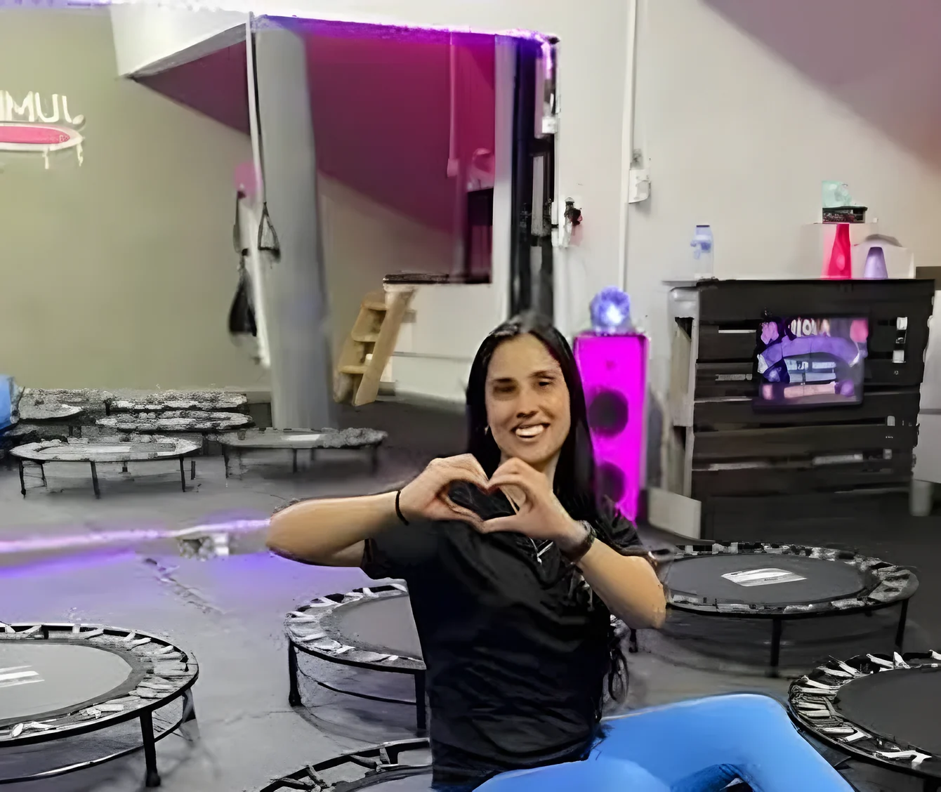 Profesora de Jump Fit sonriendo y haciendo un corazón con las manos entre las camas elásticas